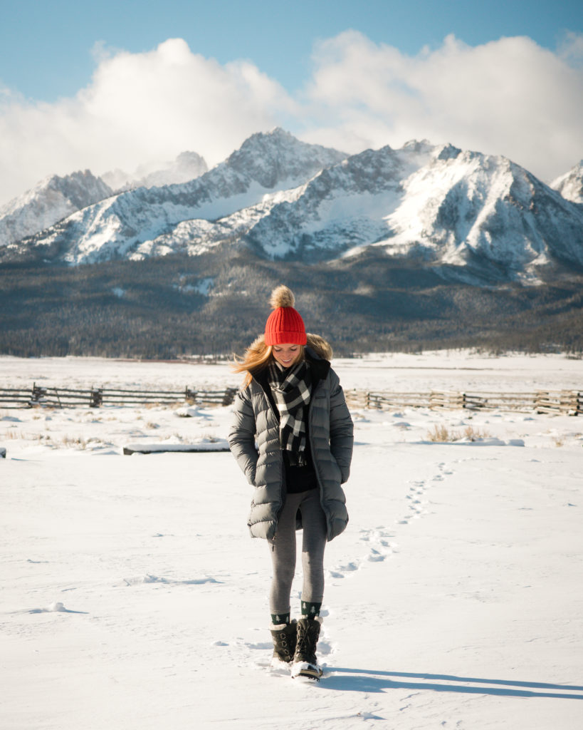 jess walking in the snow in a black down jacket and a red beanie hat