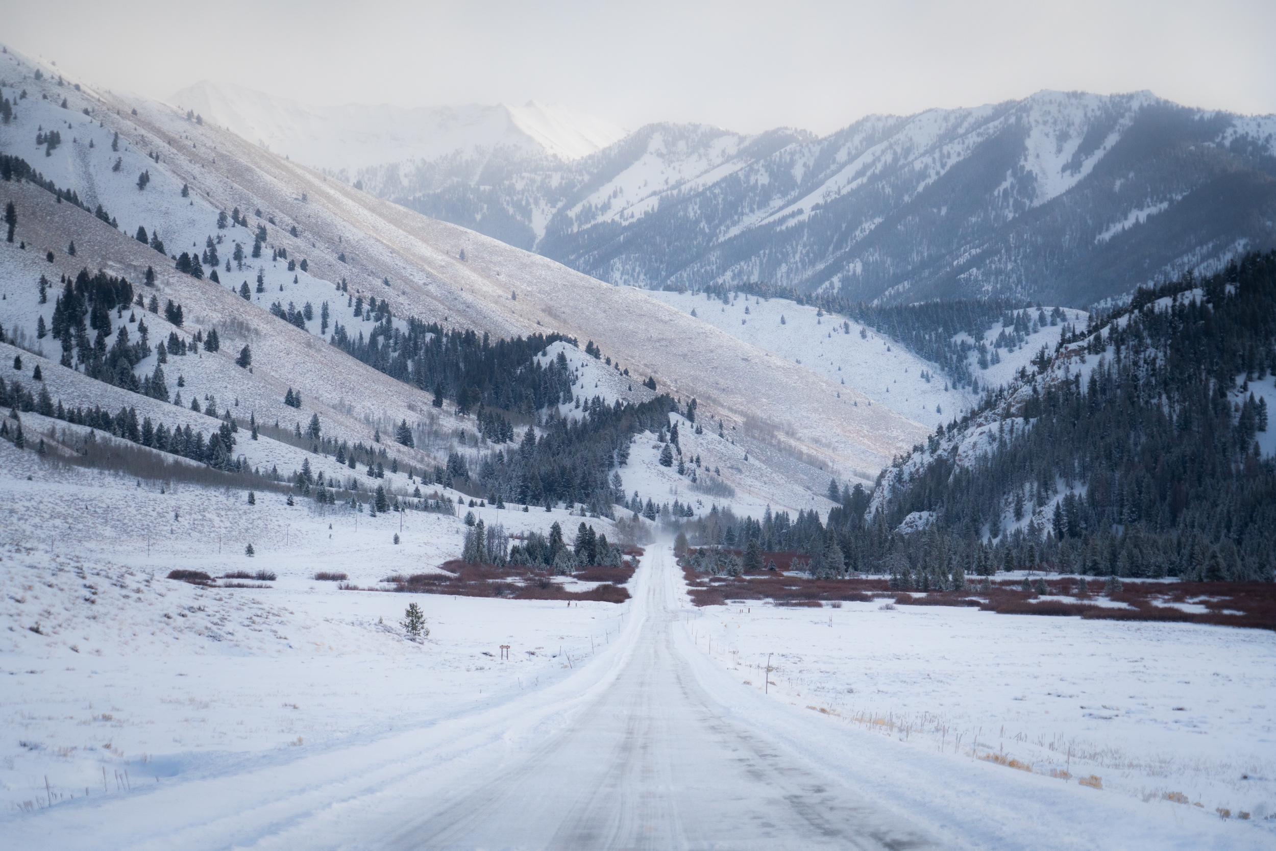 A long snow covered road disappearing into the mountain range in the distance