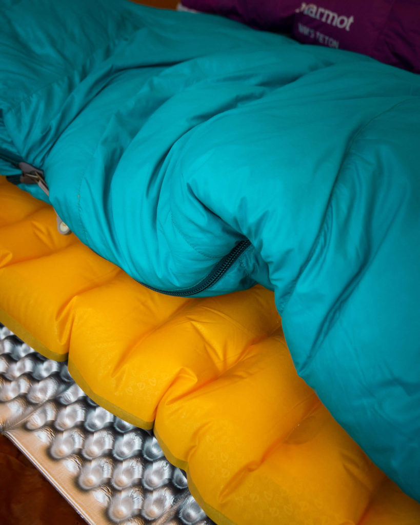 One key to staying warm at night in cold weather is creating a barrier of insulation between the ground and your body. Show In Photo:  Therm-a-Rest Foam Pad ,  NEMO Sleeping Pad ,  Marmot Women's Xenon 15° Sleeping Bag 