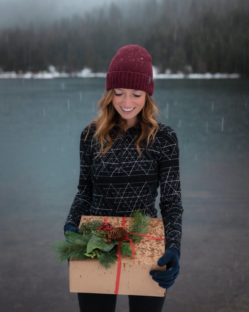Jess in the snow holding a present box with a ribbon and small wreath decoration