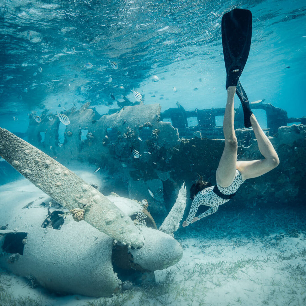 A figure wearing fins free diving towards an airplane wreck under the water in the Exumas - one of the best places to visit in the Exumas
