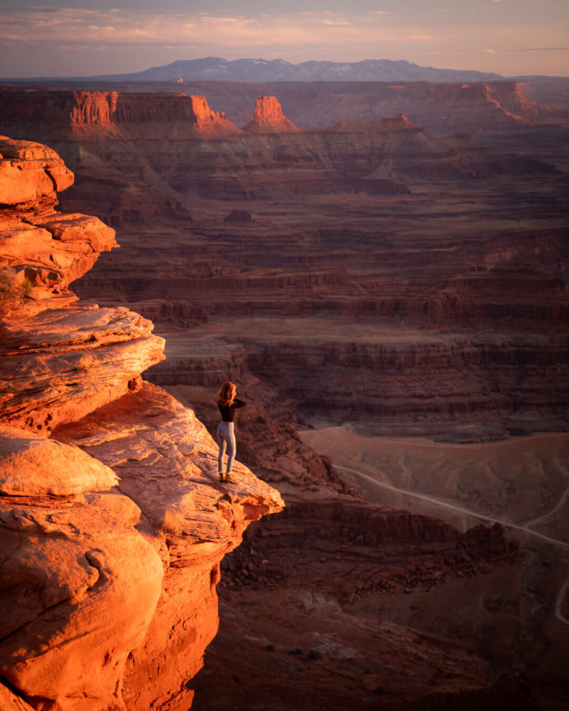 A figure standing on a rocky ledge overlooking the red rock landscape and a huge canyon in Moab, Utah