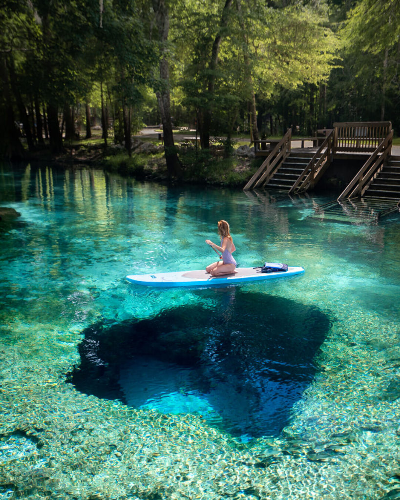 Jess kneeling on a paddleboard which is floating on a clear turquoise hot spring during a spring time trip to Florida.