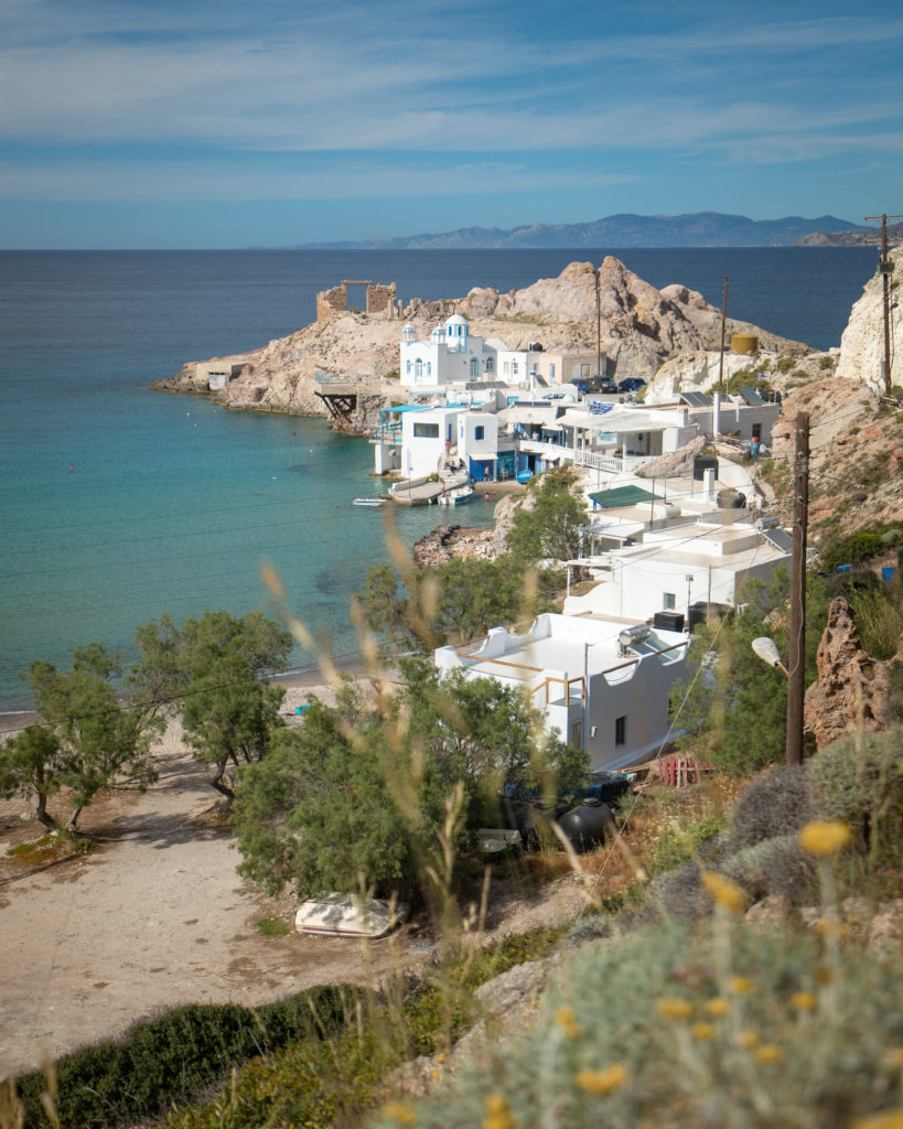 A small white washed village nestled in the rocky landscape of Milos right next to the blue sea