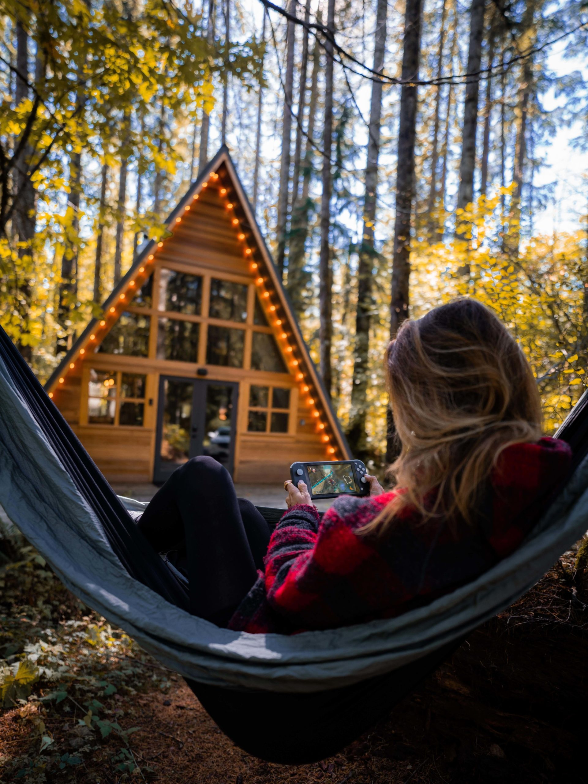 a cosy wooden a-frame cabin in a forest with Jess in a hammock in the foreground