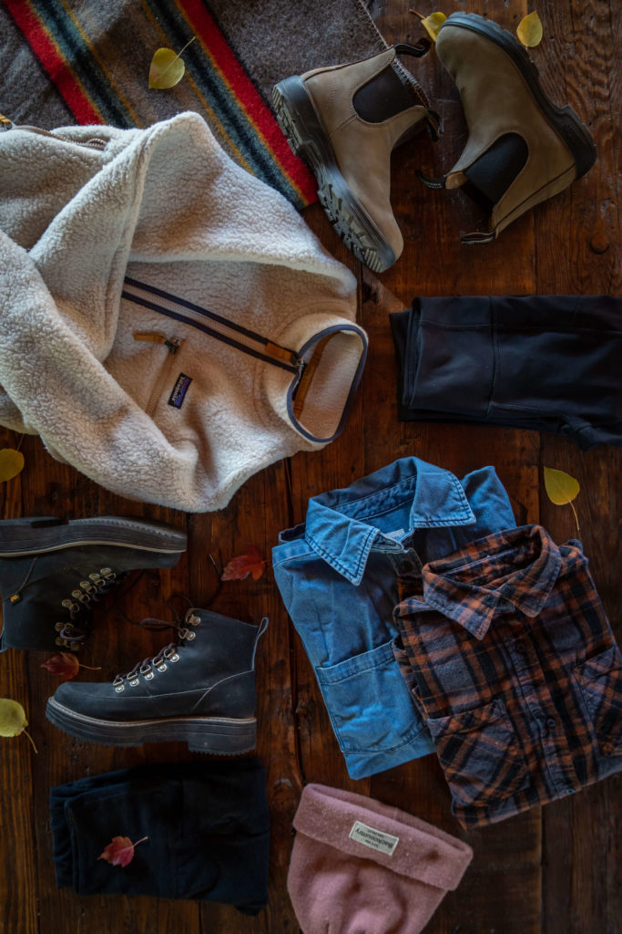 a flatlay view of outdoor gear including boots, a beanie hat, a fleece and two shirts