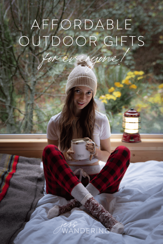 Pinnable image with overlay text that reads "Affordable outdoor gifts for everyone" with Jess sitting on a bed in pyjamas and a hat with a Yeti mug
