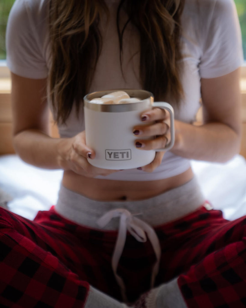 a close up image of a woman's hands holding a white Yeti camping mug
