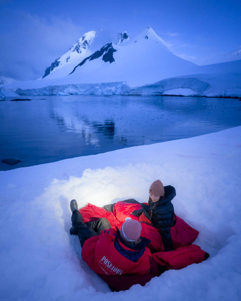 camping in Antarctica at night, two people in a dug out snow hole is red jackets and sleeping bags