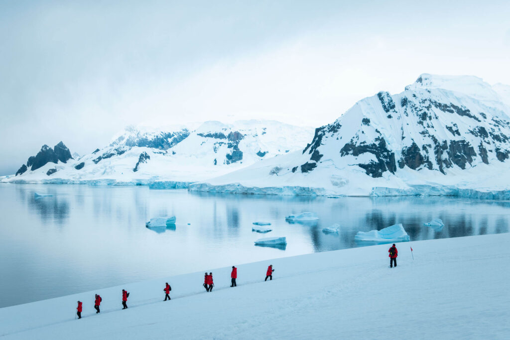 A group of people in the snow in Antarctic wearing red expedition parkas - essential clothing for what to wear in Antarctica