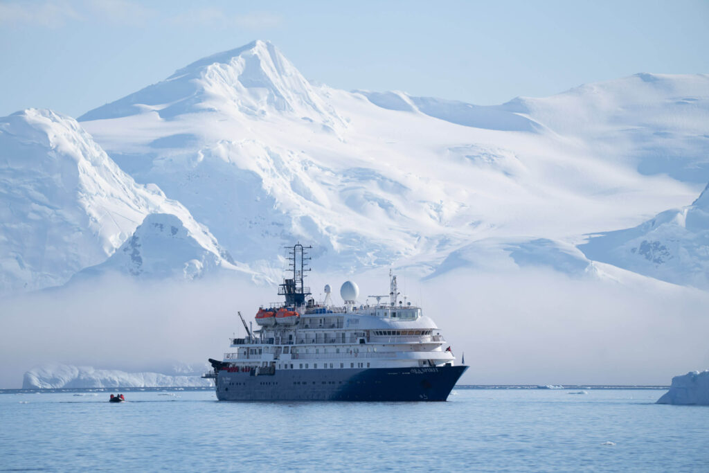 an Antarctica cruise ship waiting in the sea with snow covered mountains in the distance
