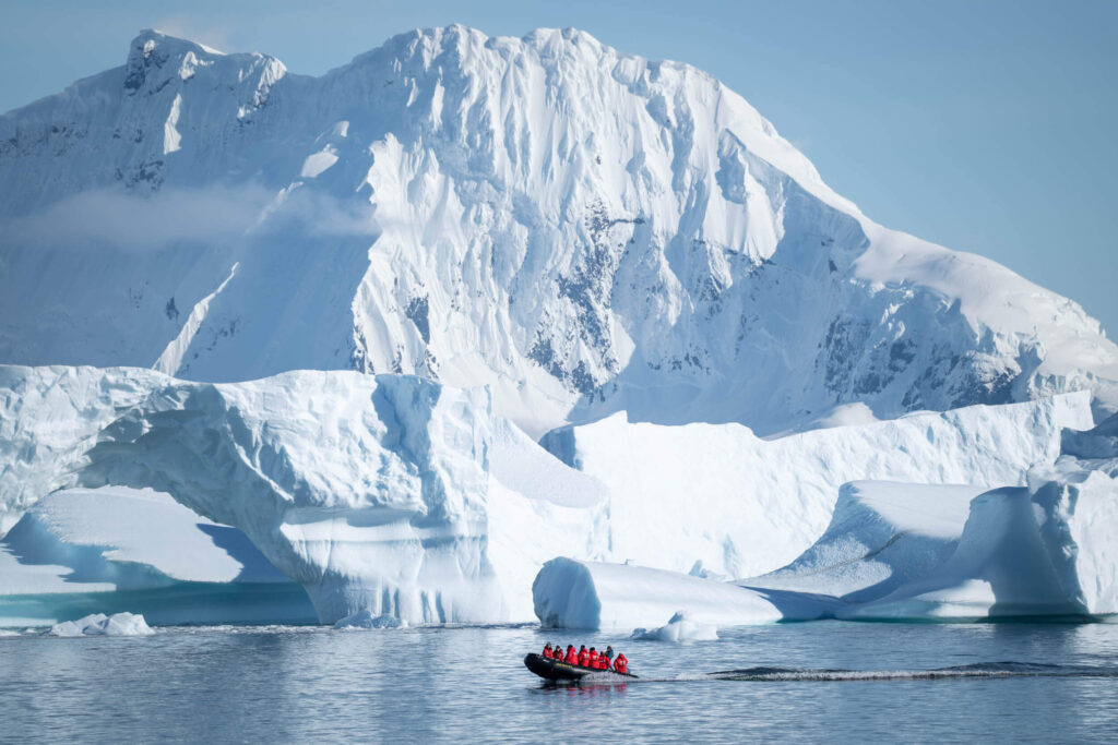 A zodiac boat out on an excursion in Antarctica with a towering mountain covered in snow 