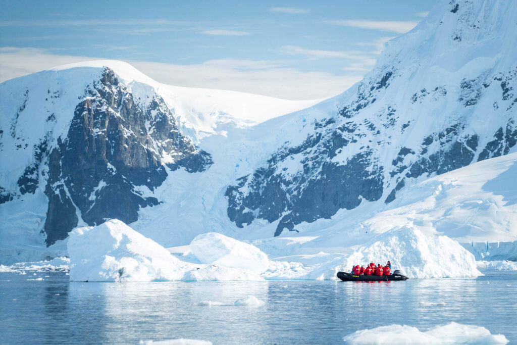 A small zodiac expedition boat with people in red jackets cruising alongside the icebergs in Antarctica