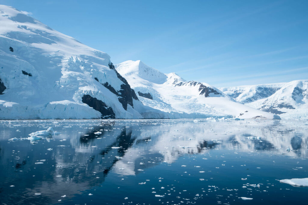 the icy dark waters of Antarctica surrounded by snowy mountains on a sunny day