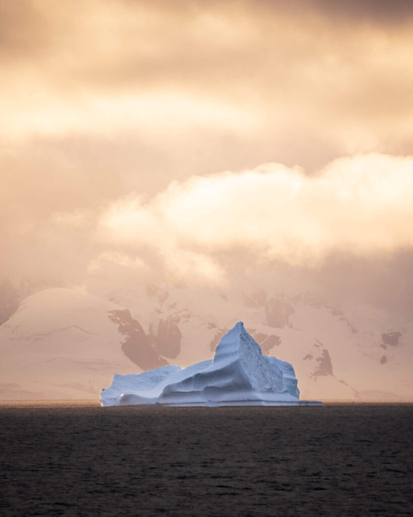 an ice berg floating in the distance at sunset in the dark water with snow covered landscape in the distance