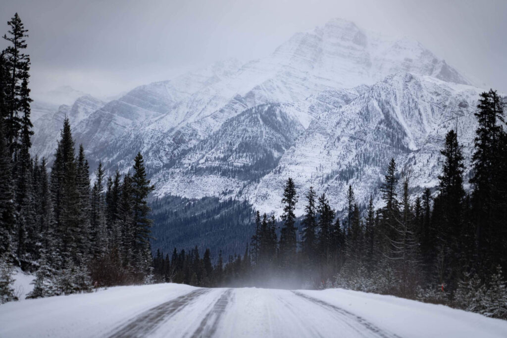 A snowy scene at Icefield Parkway looking down a snow covered road leading to a mountain in the distance - a scenic drive here is one of the best winter activities in Banff national park