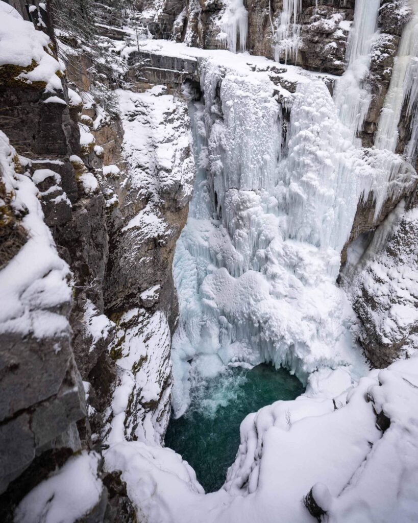 A frozen waterfall in a rocky canyon cascading into a dark green pool below