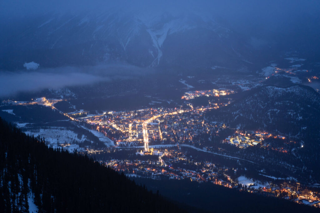 A view of a lit up town at night in the valley, seen from the top of Banff Gondola