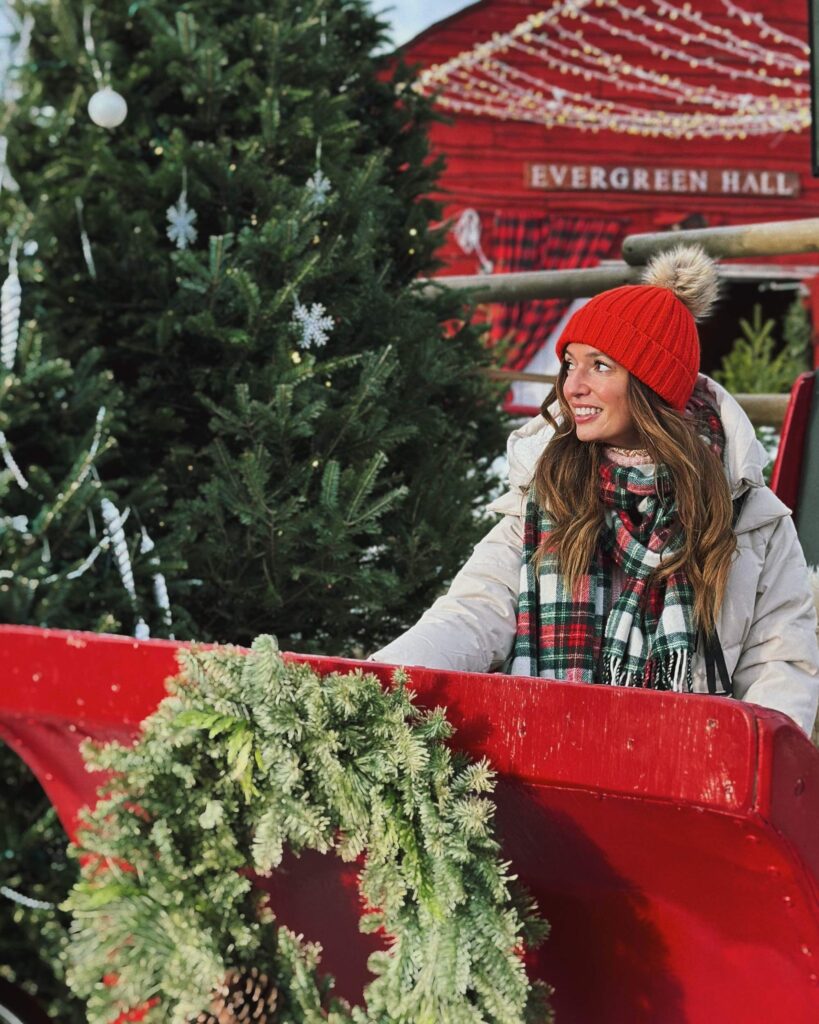 Jess in a red hat and winter clothes sitting in a red Santa sleigh
