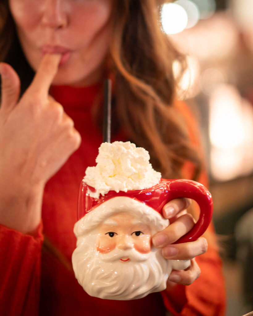Jess holding a Santa mug with whipped cream on top and licking her finger