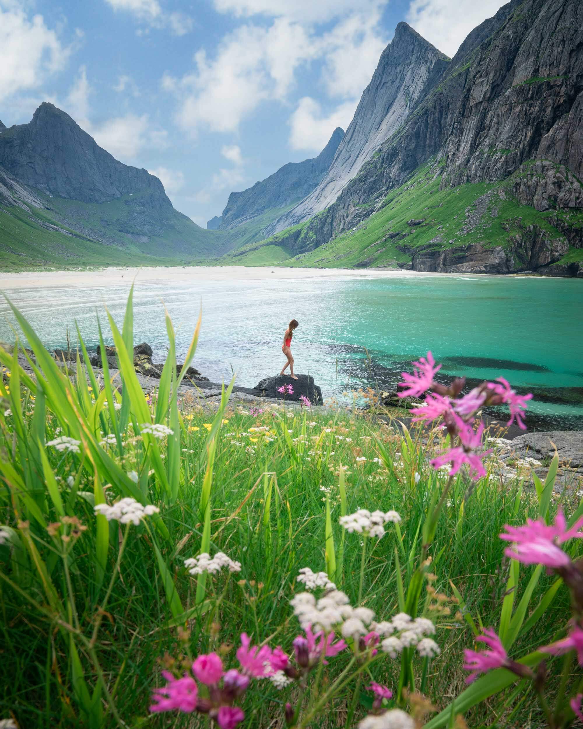 Jess Wandering standing on a rock with summer wildflowers at Horseid Beach, one of the best day hikes in Norway